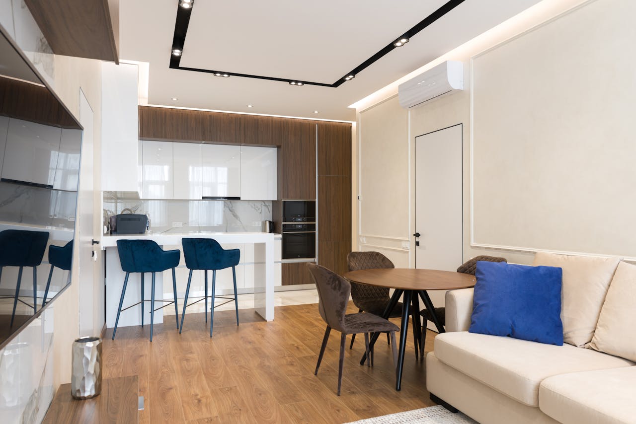 Om oss Comfortable sofa with cushions placed in front of TV in modern studio apartment with kitchen and dining zones